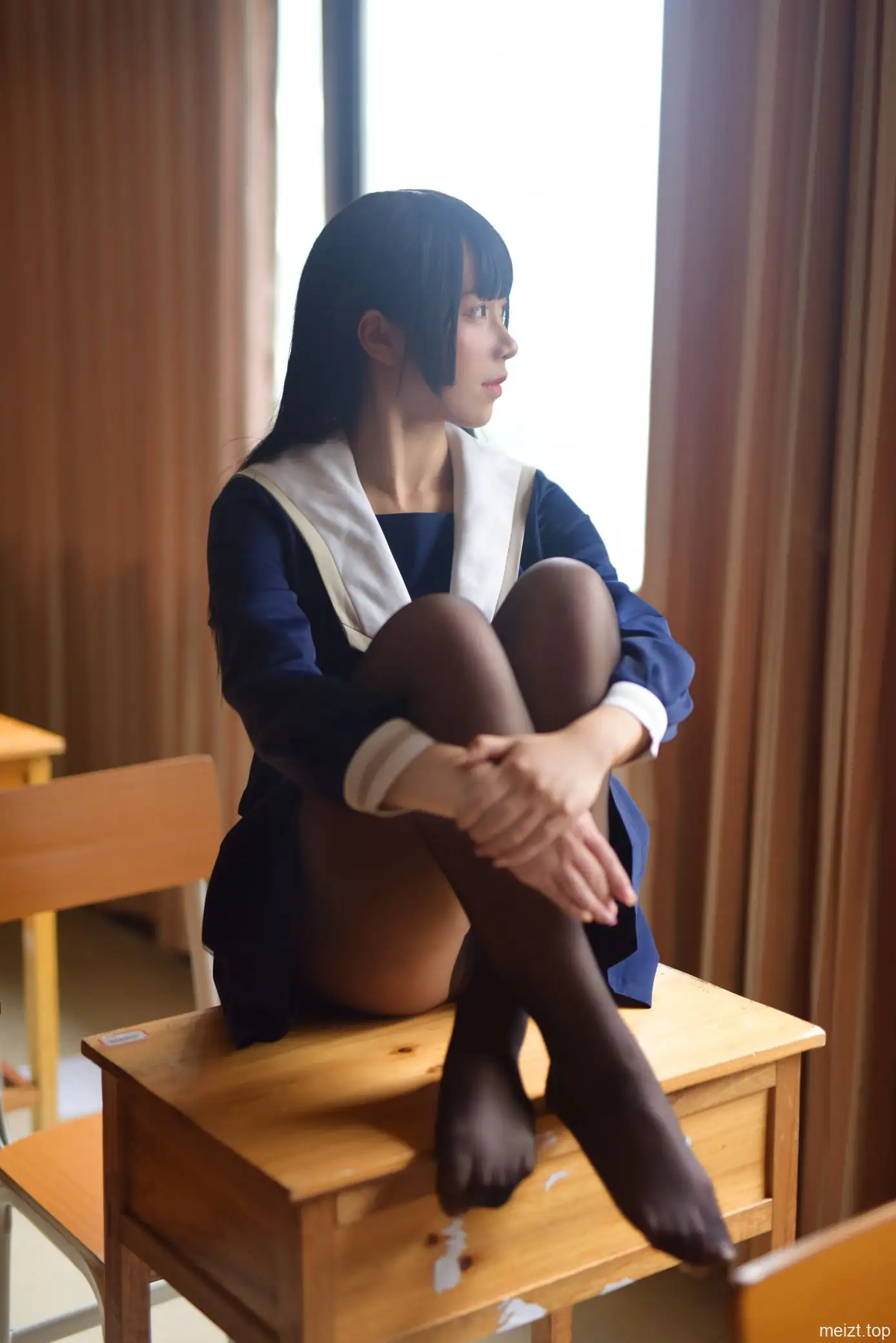 九曲Jean穿藏青水手服与黑色长袜坐在教室课桌上抱膝,身后是大面积窗光