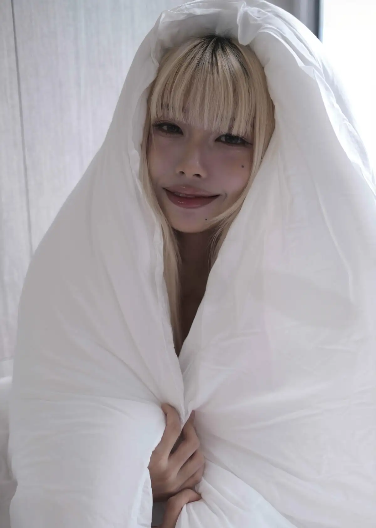 九曲Jean金色短发裹在白色被子里的近景,窗光从侧面照亮面部
