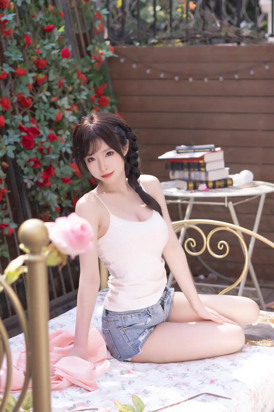清水由乃扎辫子穿白色上衣和牛仔短裤,坐在花架与木墙之间