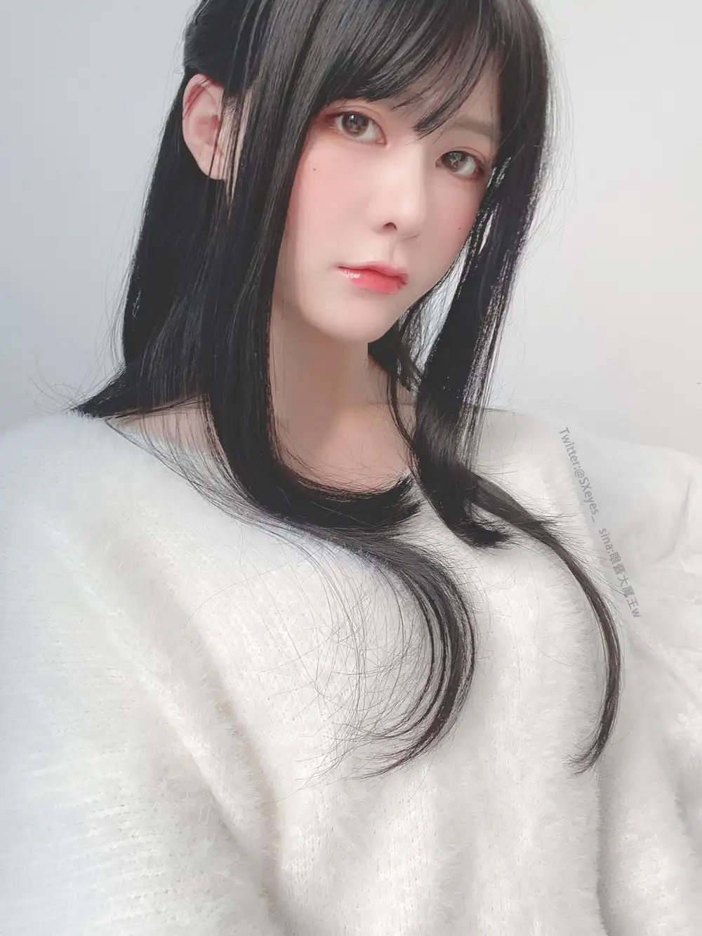 眼酱大魔王黑色长发搭配白色针织衫,浅色背景中的头肩肖像