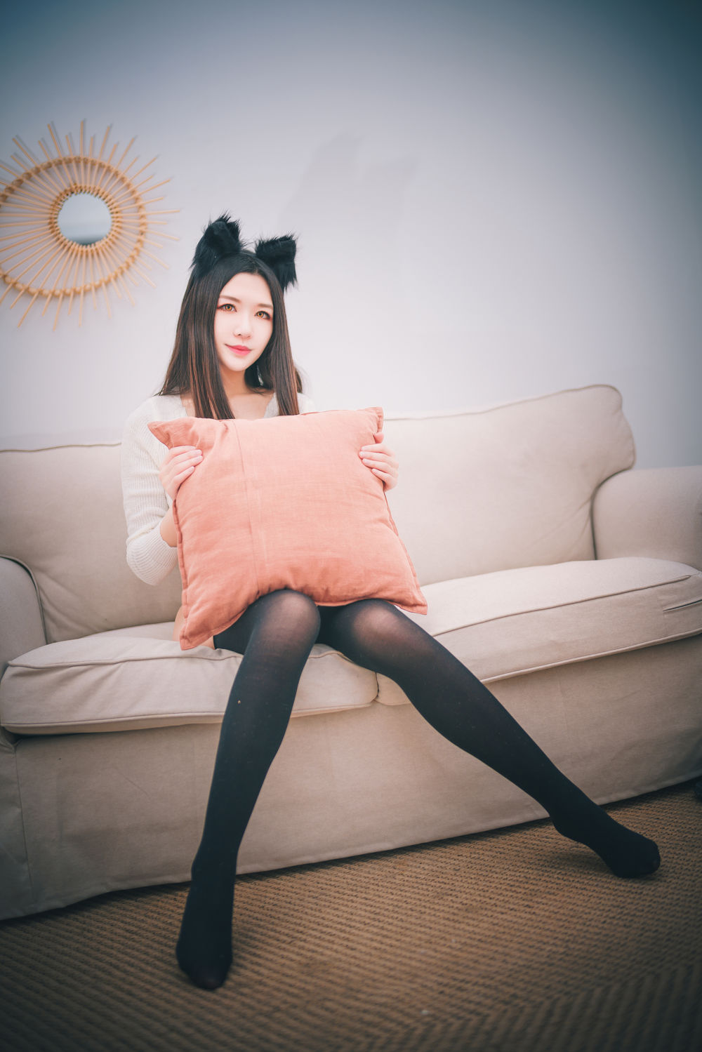 源纱希喵喵喵戴黑色猫耳穿白色针织衣和黑色长袜,抱着橘色抱枕坐在沙发上