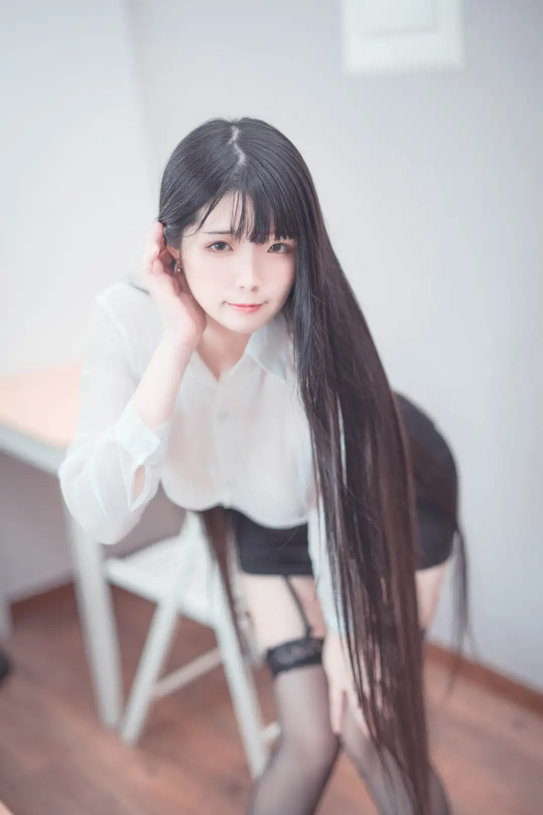 落落Raku黑色长发披肩,穿白色上衣与黑色短裙坐姿,室内浅色背景柔光近景