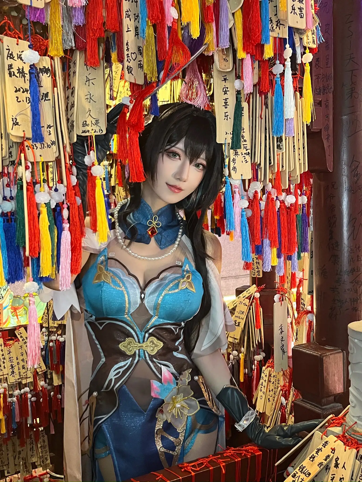弥音音黑长发带浅蓝挑染,穿蓝金刺绣高领角色服与深色手套,站在祈愿木牌与彩穗丛中 弥音音黑长发带浅蓝挑染,穿蓝金刺绣高领角色服与深色手套,站在祈愿木牌与彩穗丛中