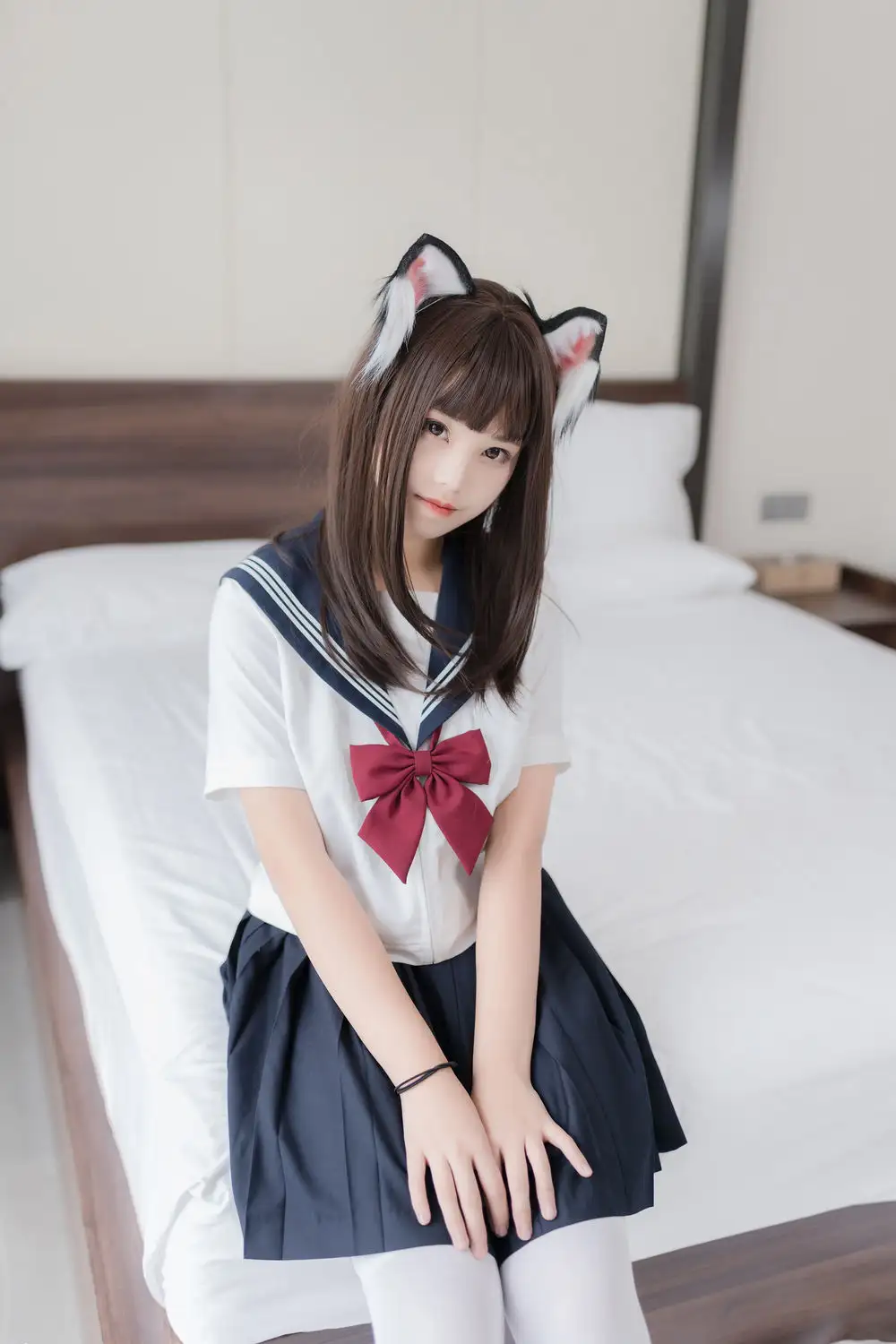 蜜汁猫裘戴猫耳穿白色水手服与深蓝裙装,坐在床边回望镜头